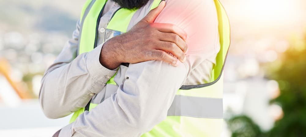 Industrial worker in a reflective vest suffering a shoulder injury, used for content about workers' compensation or personal injury settlement cases.